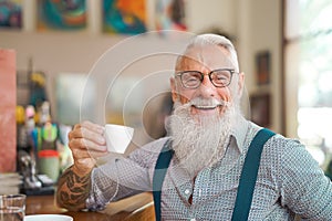 Happy smiling senior man drinking coffee in bar restaurant - Hipster trendy older male portrait
