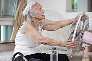 Happy smiling senior woman enjoying cooling wind from electric fan,old elderly people refreshing embracing cooling fan in sunny