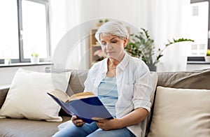 Happy smiling senior woman reading book at home