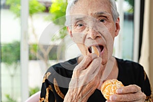 Happy smiling senior woman tasting mandarin deliciously,healthy asian old elderly opening her mouth to eat delicious organic