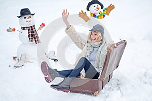 Happy smiling snow man and winter girl on sunny winter day. Winter holiday. Woman with suitcase.