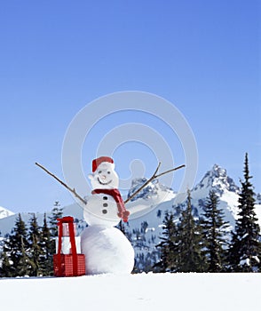 Happy, smiling snowman with Santa hat, Christmas gifts and snowy mountains in background