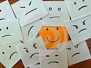 Happy smiling sticky note among unhappy, sad, angry and emotional face drawings.