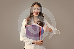 Happy smiling student or teacher with thumbs up. Teenager student girl isolated on grey background. Cheerful young woman