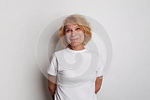 Happy smiling successful middle age woman wearing casual t-shirt standing against white studio wall banner background, portrait