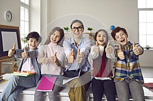 Happy smiling teacher with pupils group giving thumbs up portrait in schoolroom