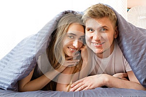 Happy smiling teen couple under blanket on bed in the morning - love relationship concept