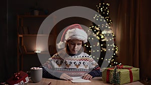 Happy smiling teen girl putting her letter and wish list in a paper envelope before sending it to Santa Claus. Christmas