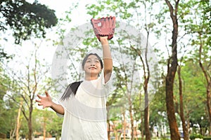 Happy smiling teenage Asian girl wearing leather glove playing baseball at public park