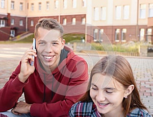 Happy smiling teenage boy talking on his phone against a group of students on the stairs near university