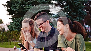 Happy smiling teenage friends laughing outside at something in smartphone or mobile phone. Three young multiracial