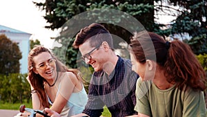 Happy smiling teenage friends laughing outside at something in smartphone or mobile phone. Three young multiracial