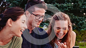 Happy smiling teenage friends laughing outside at something in smartphone or mobile phone. Three young multiracial