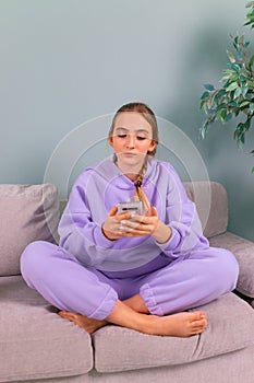 Happy smiling teenage girl with her smartphone browsing social newtwork, communicating relaxed on a couch at home