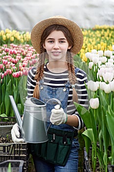 Happy smiling teenager girl in hat with watering can in blossoming tulip farm