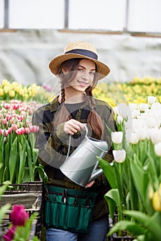 Happy smiling teenager girl in hat with watering can in blossoming tulip farm