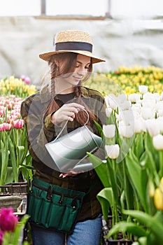 Happy smiling teenager girl in hat with watering can in blossoming tulip farm