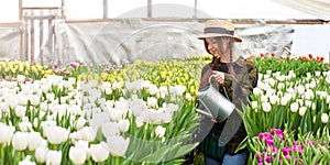 Happy smiling teenager girl in hat with watering can in blossoming tulip farm