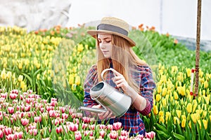 Happy smiling teenager girl in hat with watering can in blossoming tulip garden