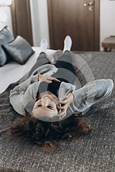 Happy smiling teenager girl talking by phone lying on her back on the bed