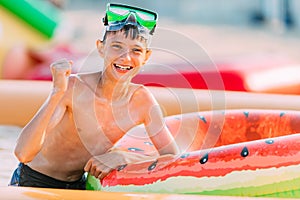 Happy smiling teenager in swimming glasses lies on the beach with an inflatable circle, and shows a winning gesture. Summer