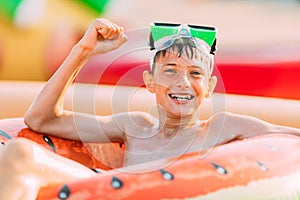 Happy smiling teenager in swimming glasses lies on the beach with an inflatable circle, and shows a winning gesture. Summer