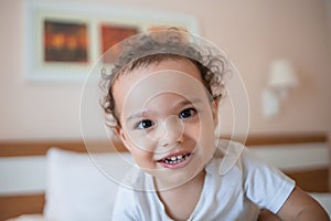 Happy smiling toddler boy on the bed looking to camera