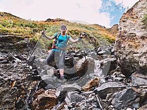 Happy smiling tourist girl backpacker crossing a mountain river in Caucasus mountains