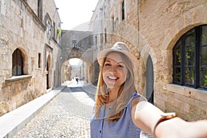 Happy smiling traveler girl taking selfie in the Street of the Knights of Rhodes city, Greece. Young female traveler visiting