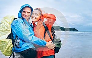 Happy smiling travelers couple in rainy day on the ocean beach