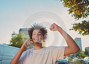 Happy smiling urban hipster young man using smart phone. African american teenager holding mobile smartphone on sunset