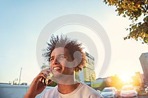 Happy smiling urban hipster young man using smart phone. African american teenager holding mobile smartphone on sunset