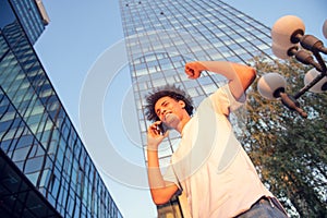 Happy smiling urban hipster young man using smart phone. African american teenager holding mobile smartphone on sunset