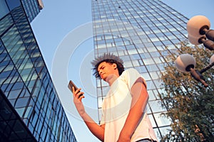 Happy smiling urban hipster young man using smart phone. African american teenager holding mobile smartphone on sunset