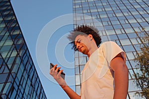 Happy smiling urban hipster young man using smart phone. African american teenager holding mobile smartphone on sunset