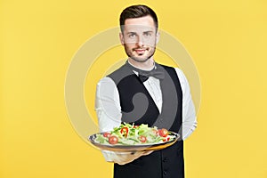 Happy smiling waiter holding plate with healthy vegetable salad ready to serve