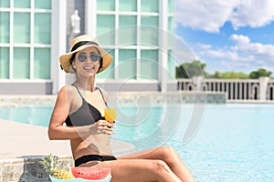 Happy smiling woman in bikini with straw hat relaxing with orange juice at poolside. beautiful female relaxing in summer time.