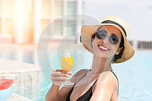 Happy smiling woman in bikini with straw hat relaxing with orange juice at poolside. beautiful female relaxing in summer time.