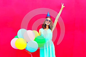 Happy smiling woman in a birthday cap having fun over an air colorful balloons pink