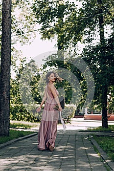 Happy and smiling woman with bouquet of flowers in a pink wedding dress and wedding ring. Running Bride, Bridesmaid. City park