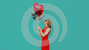 Happy smiling woman with bunch of red heart shaped balloons on blue background
