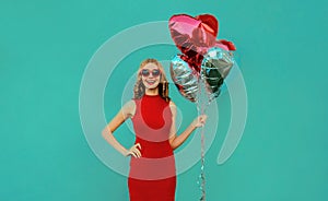 Happy smiling woman with bunch of red heart shaped balloons on blue background