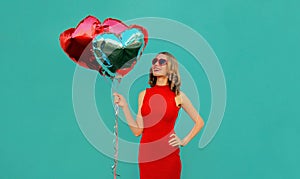 Happy smiling woman with bunch of red heart shaped balloons on blue background