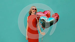 Happy smiling woman with bunch of red heart shaped balloons on blue background