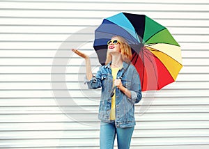 Happy smiling woman with colorful umbrella checking with outstretched hand rain on white