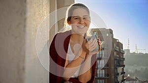 Happy smiling woman drinking tea on the balcony at morning. People relaxing, resting at home, beautiful cityscape