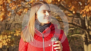 Happy Smiling Woman Enjoying Nature. Young female in red coat with hot mug standing in autumn park