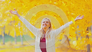 Happy smiling woman flying yellow leaves in autumn park