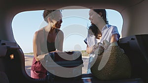 Happy smiling woman friends put bag and luggage into car trunk