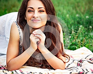 Happy smiling woman with green amazing eyes looking in camera lying on the green summer grass. Closeup